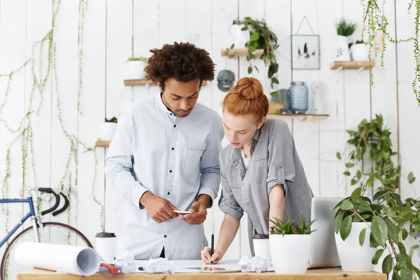 Ein ernster, konzentrierter Mann und eine ernste, konzentrierte Frau stehen in der Nähe eines Schreibtisches, umgeben von modernen Geräten.